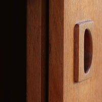 こちらの小ぶりなボードは、温かみのあるチーク材を用いたすっきりとした佇まいが魅力の北欧ビンテージ家具で、スライド扉を開くと左右に棚板付きの収納スペースが現れ、日用品や小物を効率よく整理できます。直線的な箱型の構造に、細身でテーパーの効いた脚部が軽やかな印象を添え、コンパクトながら存在感のある設計が空間に落ち着いたアクセントをもたらします。経年で深まった木肌の質感も味わい深く、リビングや玄関脇のサイド収納としても取り入れやすい一台です。