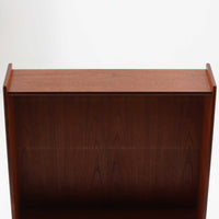 スウェーデン製のチーク材とオーク材を組み合わせたディスプレイシェルフです。幅90cmと程よいサイズ感で、上部の棚は書籍やオブジェの展示に適し、下部の引き戸収納は日用品や小物をすっきりと収めることができます。丸みを帯びた取っ手が温かみのあるアクセントとなり、北欧家具らしいシンプルで実用的なデザインを際立たせています。経年によって深みを増したチークの木目とオークのコントラストが上品な存在感を放ち、リビングや書斎の空間に落ち着いた雰囲気を添えるビンテージ家具です。