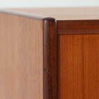 スウェーデン製のチーク材とオーク材を組み合わせたディスプレイシェルフです。幅90cmと程よいサイズ感で、上部の棚は書籍やオブジェの展示に適し、下部の引き戸収納は日用品や小物をすっきりと収めることができます。丸みを帯びた取っ手が温かみのあるアクセントとなり、北欧家具らしいシンプルで実用的なデザインを際立たせています。経年によって深みを増したチークの木目とオークのコントラストが上品な存在感を放ち、リビングや書斎の空間に落ち着いた雰囲気を添えるビンテージ家具です。