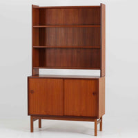 スウェーデン製のディスプレイシェルフです。上段には3段のオープンシェルフが設けられ、本や雑貨、オブジェなどを美しくディスプレイできます。下段にはスライド扉収納が備わり、内部の棚板によって整理しやすく、見せたくない収納にも便利です。チーク材の温もりある木目と、丸い掘り込み取っ手の柔らかなデザインが印象的で、北欧家具らしい穏やかな雰囲気を演出します。背面のグリーンの化粧板が空間に個性を添え、飾るアイテムをより際立たせます。本体にはチーク材、脚部にはオーク材が使用されており、素材のコントラストも魅力のひとつです。下段収納部の棚板にわずかな反りがありますが、裏返して使用することで目立たなくなります。軽やかな佇まいと実用性を兼ね備えた、北欧ビンテージらしい一台です。