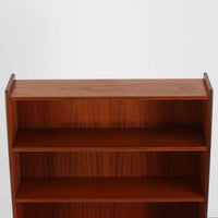 スウェーデン製のディスプレイシェルフです。上段には3段のオープンシェルフが設けられ、本や雑貨、オブジェなどを美しくディスプレイできます。下段にはスライド扉収納が備わり、内部の棚板によって整理しやすく、見せたくない収納にも便利です。チーク材の温もりある木目と、丸い掘り込み取っ手の柔らかなデザインが印象的で、北欧家具らしい穏やかな雰囲気を演出します。背面のグリーンの化粧板が空間に個性を添え、飾るアイテムをより際立たせます。本体にはチーク材、脚部にはオーク材が使用されており、素材のコントラストも魅力のひとつです。下段収納部の棚板にわずかな反りがありますが、裏返して使用することで目立たなくなります。軽やかな佇まいと実用性を兼ね備えた、北欧ビンテージらしい一台です。