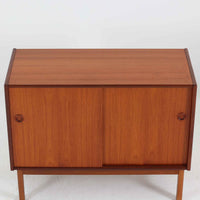 スウェーデン製のディスプレイシェルフです。上段には3段のオープンシェルフが設けられ、本や雑貨、オブジェなどを美しくディスプレイできます。下段にはスライド扉収納が備わり、内部の棚板によって整理しやすく、見せたくない収納にも便利です。チーク材の温もりある木目と、丸い掘り込み取っ手の柔らかなデザインが印象的で、北欧家具らしい穏やかな雰囲気を演出します。背面のグリーンの化粧板が空間に個性を添え、飾るアイテムをより際立たせます。本体にはチーク材、脚部にはオーク材が使用されており、素材のコントラストも魅力のひとつです。下段収納部の棚板にわずかな反りがありますが、裏返して使用することで目立たなくなります。軽やかな佇まいと実用性を兼ね備えた、北欧ビンテージらしい一台です。