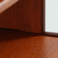 スウェーデン製のディスプレイシェルフです。上段には3段のオープンシェルフが設けられ、本や雑貨、オブジェなどを美しくディスプレイできます。下段にはスライド扉収納が備わり、内部の棚板によって整理しやすく、見せたくない収納にも便利です。チーク材の温もりある木目と、丸い掘り込み取っ手の柔らかなデザインが印象的で、北欧家具らしい穏やかな雰囲気を演出します。背面のグリーンの化粧板が空間に個性を添え、飾るアイテムをより際立たせます。本体にはチーク材、脚部にはオーク材が使用されており、素材のコントラストも魅力のひとつです。下段収納部の棚板にわずかな反りがありますが、裏返して使用することで目立たなくなります。軽やかな佇まいと実用性を兼ね備えた、北欧ビンテージらしい一台です。