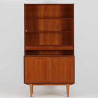 スウェーデン製のディスプレイシェルフです。上部は高さ調整可能な棚板が設けられており、書籍やオブジェの収納・展示に最適です。中央には小引き出しが2杯備わり、カトラリーや小物の整理にも便利。下部には扉付きの収納スペースがあり、日用品をすっきりと収納できます。素材にはチーク(本体)・オーク(脚の幕板)・ビーチ(脚)の3種の木材が用いられ、異なる木目のコントラストが美しい仕上がりです。北欧家具らしい温もりと実用性を兼ね備えた一台で、リビングやダイニング、書斎など幅広いシーンに調和します。