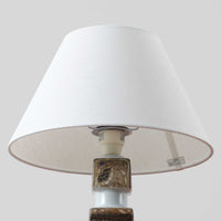 Nils Thorssonがデザインし、Royal Copenhagen社から発表された「BACA」シリーズのテーブルランプは、高さ38cmのバランスの取れたサイズ感で、北欧ビンテージらしい存在感を放ちます。陶磁器製のベースには細やかな装飾模様が施され、グラフィカルでありながら落ち着いた色調が空間に洗練された雰囲気を添えます。リネンシェードを透過する柔らかな光が温もりを演出し、リビングやベッドサイドに最適です。年月を経て深みを増した質感と工芸的な美しさを楽しめる一点物です。