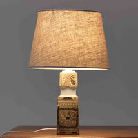 Nils Thorssonがデザインし、Royal Copenhagen社から発表された「BACA」シリーズのテーブルランプは、高さ39cmのバランスの取れたサイズ感で、北欧ビンテージらしい存在感を放ちます。陶磁器製のベースには細やかな装飾模様が施され、グラフィカルでありながら落ち着いた色調が空間に洗練された雰囲気を添えます。リネンシェードを透過する柔らかな光が温もりを演出し、リビングやベッドサイドに最適です。年月を経て深みを増した質感と工芸的な美しさを楽しめる一点物です。