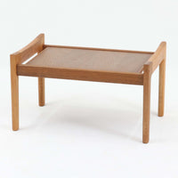 Hans J. Wegnerがデザインし、Getamaが製作したGE290オットマンの希少なサイドテーブル兼用タイプです。オーク材の美しい木目を活かしたフレームは、丸みを帯びたアーム状の意匠が印象的で、安定感のある堅牢な構造が魅力。クッションを外せばトレーテーブルとしても使用できる実用的な設計です。本品はGetama社の刻印が入る以前の古いタイプで、初期モデルならではの佇まいも価値を高めています。ラウンジチェアと合わせてはもちろん、単体でも存在感を放つ北欧ビンテージの逸品です。クッション内部にはビンテージ品ならではのスプリングが内包されています。