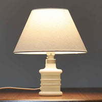 Sidse Werner(シセ・ヴェルナー)がデザインし、Holmegaard(ホルムガード)より製造されたテーブルランプ「Apoteker」です。高さ29cmと小ぶりなサイズで、艶やかなホワイトガラスのベースが柔らかな印象を与えます。リネンシェードを通した光は優しく拡散し、ナチュラルな雰囲気を演出。シンプルでありながら彫刻的なフォルムが存在感を放ち、ベッドサイドやデスク、リビングのサイドテーブルなど様々な空間で活躍します。北欧デザインの温もりを感じられるビンテージ照明です。