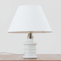 Sidse Werner(シセ・ヴェルナー)がデザインし、Holmegaard(ホルムガード)より製造されたテーブルランプ「Apoteker」です。高さ29cmと小ぶりなサイズで、艶やかなホワイトガラスのベースが柔らかな印象を与えます。リネンシェードを通した光は優しく拡散し、ナチュラルな雰囲気を演出。シンプルでありながら彫刻的なフォルムが存在感を放ち、ベッドサイドやデスク、リビングのサイドテーブルなど様々な空間で活躍します。北欧デザインの温もりを感じられるビンテージ照明です。