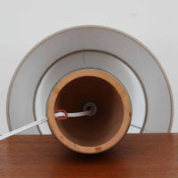 デンマーク製のテーブルランプは、高さ36cmとコンパクトで扱いやすく、陶磁器ベースには深みのある釉薬と素朴な質感が調和しています。胴部には幾何学的なレリーフが施され、落ち着いた佇まいの中に個性が光ります。リネンシェードを透過する柔らかな光が空間に温もりを与え、リビングや寝室のアクセントとしても最適です。メーカー不詳ながら、スタジオポタリーならではの職人技と一点物の味わいを感じられる北欧ビンテージ品です。
