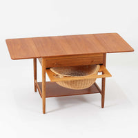 ハンス・J・ウェグナーが手がけ、Andreas Tuck社より製作されたAT33ソーイングテーブルは、天板を広げられる独創的な構造と実用性を兼ね備えた北欧ビンテージを代表する一台です。中央には引き出しと仕切り付き収納、下部にはラタンバスケットを備え、道具をすっきりと収められる設計が魅力。AT33は複数の素材構成で展開されたモデルですが、こちらは天板にチーク突板材、脚部にオーク無垢材を用いた仕様で、素材のコントラストと軽やかな佇まいが特徴です。異素材を巧みに組み合わせた構造と端正なプロポーションは、使うほどに職人技と経年変化の美しさを実感できます。