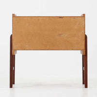 チーク材を用いた小ぶりなキャビネットは、直線を基調としつつ柔らかな丸みを持たせた側板と脚部のラインが印象的な北欧ビンテージ家具です。前板一枚で構成されたフラップ扉には掘り込み式の取っ手が設けられ、開閉時の所作も美しく、内部には実用的な収納棚を備えています。幅69cmと取り入れやすいサイズ感で、リビングや玄関、ベッドサイドの収納としても活躍し、経年により深みを増したチーク材の木目と職人技が静かな存在感を放つ一台です。