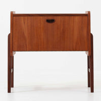 チーク材を用いた小ぶりなキャビネットは、直線を基調としつつ柔らかな丸みを持たせた側板と脚部のラインが印象的な北欧ビンテージ家具です。前板一枚で構成されたフラップ扉には掘り込み式の取っ手が設けられ、開閉時の所作も美しく、内部には実用的な収納棚を備えています。幅69cmと取り入れやすいサイズ感で、リビングや玄関、ベッドサイドの収納としても活躍し、経年により深みを増したチーク材の木目と職人技が静かな存在感を放つ一台です。