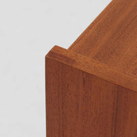 チーク材を用いた小ぶりなキャビネットは、直線を基調としつつ柔らかな丸みを持たせた側板と脚部のラインが印象的な北欧ビンテージ家具です。前板一枚で構成されたフラップ扉には掘り込み式の取っ手が設けられ、開閉時の所作も美しく、内部には実用的な収納棚を備えています。幅69cmと取り入れやすいサイズ感で、リビングや玄関、ベッドサイドの収納としても活躍し、経年により深みを増したチーク材の木目と職人技が静かな存在感を放つ一台です。