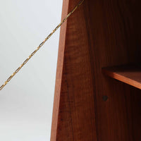 チーク材を用いた小ぶりなキャビネットは、直線を基調としつつ柔らかな丸みを持たせた側板と脚部のラインが印象的な北欧ビンテージ家具です。前板一枚で構成されたフラップ扉には掘り込み式の取っ手が設けられ、開閉時の所作も美しく、内部には実用的な収納棚を備えています。幅69cmと取り入れやすいサイズ感で、リビングや玄関、ベッドサイドの収納としても活躍し、経年により深みを増したチーク材の木目と職人技が静かな存在感を放つ一台です。