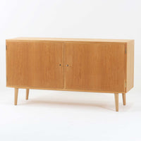 Poul Hundevadが手がけ、Hundevad & Coより製作されたキャビネットです。オーク材の端正な木目を活かしたフラットな扉構成と、細身のテーパードレッグが北欧モダンらしい軽やかさを演出します。内部は可動棚と可動式の浅型トレイを備え、書類や食器、小物まで用途に応じた整理が可能。天板下の構造や金物の収まりにも丁寧な作りが感じられ、長年の使用で深みを増した素材感がビンテージならではの魅力として空間に静かな存在感を添えます。