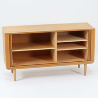 Poul Hundevadがデザインし、Hundevad & Coより製作された蛇腹仕様のサイドボードです。オーク材の穏やかで上品な木目を活かした外観に、横方向へ滑らかに開閉する蛇腹扉を組み合わせた、機能美あふれる一台。扉の開閉時に前後のスペースを取らない構造は、動線を妨げず実用性にも優れています。内部は棚板構成で収納力が高く、食器や書類、リビング周りの小物まで幅広く対応。細身の脚部が全体を軽やかに引き締め、経年によって深みを増した素材感が北欧ビンテージならではの静かな存在感を空間にもたらします。