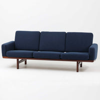 こちらは、ウェグナーデザインの人気モデル、GE236の3人掛けソファです。後ろ姿が非常に美しいため、あえて壁に寄せず背面を見せる配置もおすすめです。クッション内部にはスプリングが内蔵されており、座り心地も良好です。さらに、こちらは現地でも希少なアフロモシア材(通称アフリカンチーク)が使用された特別なモデルです。GE236のチーク材仕様として一般的に認識されているのは、このアフロモシア材が使用されたモデルを指します。GETAMA社の刻印も確認できます。