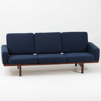 こちらは、ウェグナーデザインの人気モデル、GE236の3人掛けソファです。後ろ姿が非常に美しいため、あえて壁に寄せず背面を見せる配置もおすすめです。クッション内部にはスプリングが内蔵されており、座り心地も良好です。さらに、こちらは現地でも希少なアフロモシア材(通称アフリカンチーク)が使用された特別なモデルです。GE236のチーク材仕様として一般的に認識されているのは、このアフロモシア材が使用されたモデルを指します。GETAMA社の刻印も確認できます。