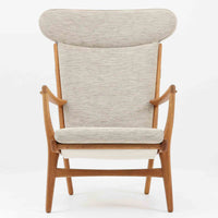 Hans J. Wegnerがデザインし、AP Stolenが製作したAP15ハイバックシングルソファです。オーク材の滑らかな木肌を活かしたフレームに、包み込むような背とヘッドレストを備えた優美なフォルムが印象的。彫刻的なアーム形状や前後に傾斜した脚部など、随所にウェグナーらしい造形美が感じられます。ホワイト系の色味が空間を明るく上品な印象に整えます。ゆったりと身体を預けられる快適な座り心地と、経年で深みを増した木部の風合いが格調ある雰囲気をもたらす北欧ビンテージの名品です。