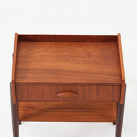 デンマーク製のサイドチェストです。チーク材ならではの温かみある木目と落ち着いた色合いが美しく、側板を立ち上げた天板形状がさりげないデザインアクセントになっています。引き出しには手掛けとして一体成形された取っ手があしらわれ、滑らかな開閉とすっきりとした正面意匠を両立しています。幅52cmの扱いやすいサイズ感で、ベッドサイドやソファ脇、玄関先などにも取り入れやすく、下段の棚板は本や小物の収納にも便利です。経年変化によって深みを増したチークの表情が、ビンテージならではの落ち着いた存在感を空間にもたらします。