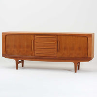 Johannes Andersenがデザインし、C.F.C. Silkeborgが製作した幅200cmのサイドボードです。チーク材の豊かな木目を活かした滑らかな曲面フレームと、横へ流れるように開閉する蛇腹扉が印象的で、端正さの中に軽やかなリズムを生み出します。中央の4段引き出しと両側の収納スペースにより高い収納力を備え、内部の棚板は可動式で実用性も良好。すらりと伸びる脚部が全体に洗練された印象を与え、空間に北欧ビンテージならではの気品と存在感をもたらします。