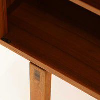 レナート・ベンダーがデザインし、Ulferts Mobler社により製作されたCoronaキャビネットは、小ぶりなサイズ感と端正な佇まいが魅力の北欧ビンテージ家具です。チーク材の美しい木目を活かしたシンプルな箱型構造に、脚部の控えめな意匠が軽やかさを添えています。取っ手部分には異素材となるローズウッドが用いられており、チーク材とのコントラストがさりげないアクセントとして全体の表情を引き締めています。内部は使いやすい収納空間を備え、食器や書類、小物類の整理に適しており、リビングや書斎、玄関周りなど幅広いシーンで活躍します。年月を経て深みを増した素材感と、丁寧な作りが感じられる一台です。