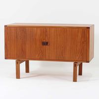 レナート・ベンダーがデザインし、Ulferts Mobler社により製作されたCoronaキャビネットは、小ぶりなサイズ感と端正な佇まいが魅力の北欧ビンテージ家具です。チーク材の美しい木目を活かしたシンプルな箱型構造に、脚部の控えめな意匠が軽やかさを添えています。取っ手部分には異素材となるローズウッドが用いられており、チーク材とのコントラストがさりげないアクセントとして全体の表情を引き締めています。内部は使いやすい収納空間を備え、食器や書類、小物類の整理に適しており、リビングや書斎、玄関周りなど幅広いシーンで活躍します。年月を経て深みを増した素材感と、丁寧な作りが感じられる一台です。