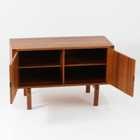 レナート・ベンダーがデザインし、Ulferts Mobler社により製作されたCoronaキャビネットは、小ぶりなサイズ感と端正な佇まいが魅力の北欧ビンテージ家具です。チーク材の美しい木目を活かしたシンプルな箱型構造に、脚部の控えめな意匠が軽やかさを添えています。取っ手部分には異素材となるローズウッドが用いられており、チーク材とのコントラストがさりげないアクセントとして全体の表情を引き締めています。内部は使いやすい収納空間を備え、食器や書類、小物類の整理に適しており、リビングや書斎、玄関周りなど幅広いシーンで活躍します。年月を経て深みを増した素材感と、丁寧な作りが感じられる一台です。