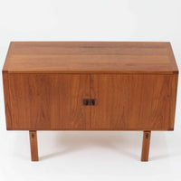 レナート・ベンダーがデザインし、Ulferts Mobler社により製作されたCoronaキャビネットは、小ぶりなサイズ感と端正な佇まいが魅力の北欧ビンテージ家具です。チーク材の美しい木目を活かしたシンプルな箱型構造に、脚部の控えめな意匠が軽やかさを添えています。取っ手部分には異素材となるローズウッドが用いられており、チーク材とのコントラストがさりげないアクセントとして全体の表情を引き締めています。内部は使いやすい収納空間を備え、食器や書類、小物類の整理に適しており、リビングや書斎、玄関周りなど幅広いシーンで活躍します。年月を経て深みを増した素材感と、丁寧な作りが感じられる一台です。