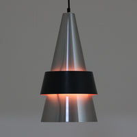 Jo HammerborgがFog & Morupのために手掛けた「Corona」は、直径22cmとコンパクトながら全高45cmと縦にしっかりとした存在感を持つアルミ×スチール製ペンダントライトで、上下に伸びる円錐形フォルムと中央のブラックバンドが彫刻的な印象を与える北欧ビンテージ品です。光源を囲む二重構造によって眩しさを抑えつつ下方向へ明かりを集中的に落とす設計となっており、ダイニングやカウンター上での1灯使用はもちろん、複数灯を並べても空間にリズムを生み出します。経年で深まった素材の風合いがハーマボーらしいモダンな佇まいを際立たせ、空間のアクセントとしても十分な存在感を発揮します。