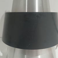 Jo HammerborgがFog & Morupのために手掛けた「Corona」は、直径22cmとコンパクトながら全高45cmと縦にしっかりとした存在感を持つアルミ×スチール製ペンダントライトで、上下に伸びる円錐形フォルムと中央のブラックバンドが彫刻的な印象を与える北欧ビンテージ品です。光源を囲む二重構造によって眩しさを抑えつつ下方向へ明かりを集中的に落とす設計となっており、ダイニングやカウンター上での1灯使用はもちろん、複数灯を並べても空間にリズムを生み出します。経年で深まった素材の風合いがハーマボーらしいモダンな佇まいを際立たせ、空間のアクセントとしても十分な存在感を発揮します。