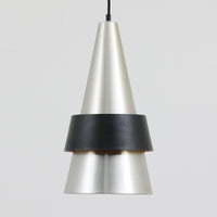 Jo HammerborgがFog & Morupのために手掛けた「Corona」は、直径22cmとコンパクトながら全高45cmと縦にしっかりとした存在感を持つアルミ×スチール製ペンダントライトで、上下に伸びる円錐形フォルムと中央のブラックバンドが彫刻的な印象を与える北欧ビンテージ品です。光源を囲む二重構造によって眩しさを抑えつつ下方向へ明かりを集中的に落とす設計となっており、ダイニングやカウンター上での1灯使用はもちろん、複数灯を並べても空間にリズムを生み出します。経年で深まった素材の風合いがハーマボーらしいモダンな佇まいを際立たせ、空間のアクセントとしても十分な存在感を発揮します。