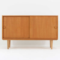 Domino Moblerが製作したデンマーク製ボードです。オーク材の明るく穏やかな木目を活かした端正なフレームです。引き戸構造により省スペースで使いやすく、内部には棚板を備え日用品や書類、食器などをすっきりと収納可能。幅122cmのバランスの取れたサイズ感で、リビングやダイニングのサイドキャビネットとしても活躍します。経年で味わいを増した木肌が空間に温もりと北欧ビンテージらしい趣を添える一品です。