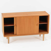 Domino Moblerが製作したデンマーク製ボードです。オーク材の明るく穏やかな木目を活かした端正なフレームです。引き戸構造により省スペースで使いやすく、内部には棚板を備え日用品や書類、食器などをすっきりと収納可能。幅122cmのバランスの取れたサイズ感で、リビングやダイニングのサイドキャビネットとしても活躍します。経年で味わいを増した木肌が空間に温もりと北欧ビンテージらしい趣を添える一品です。