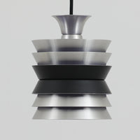 Carl ThoreがGranhaga Metallindustriで手掛けた直径15cmの小ぶりなペンダントライトで、段状に重ねたアルミシェードが光を柔らかく拡散し、点灯時には上下方向へ美しいグラデーションを生み出す北欧ビンテージ品です。繊細なヘアライン仕上げとブラックパーツのコントラストがモダンな印象を与え、キッチンカウンターや小空間のアクセント照明としてはもちろん、複数灯を並べたコーディネートにも最適です。コンパクトながら彫刻的なフォルムが存在感を放ち、経年で深まった質感がビンテージならではの魅力を際立たせています。