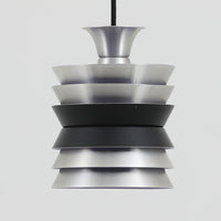 Carl ThoreがGranhaga Metallindustriで手掛けた直径15cmの小ぶりなペンダントライトで、段状に重ねたアルミシェードが光を柔らかく拡散し、点灯時には上下方向へ美しいグラデーションを生み出す北欧ビンテージ品です。繊細なヘアライン仕上げとブラックパーツのコントラストがモダンな印象を与え、キッチンカウンターや小空間のアクセント照明としてはもちろん、複数灯を並べたコーディネートにも最適です。コンパクトながら彫刻的なフォルムが存在感を放ち、経年で深まった質感がビンテージならではの魅力を際立たせています。