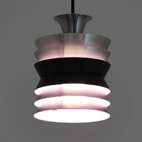 Carl ThoreがGranhaga Metallindustriで手掛けた直径15cmの小ぶりなペンダントライトで、段状に重ねたアルミシェードが光を柔らかく拡散し、点灯時には上下方向へ美しいグラデーションを生み出す北欧ビンテージ品です。繊細なヘアライン仕上げとブラックパーツのコントラストがモダンな印象を与え、キッチンカウンターや小空間のアクセント照明としてはもちろん、複数灯を並べたコーディネートにも最適です。コンパクトながら彫刻的なフォルムが存在感を放ち、経年で深まった質感がビンテージならではの魅力を際立たせています。