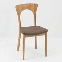 Niels Koefoedが1957年にデザインし、現在はCaso Furnitureより復刻製作されているモデル「Peter」のダイニングチェアです。オーク材の美しい木目を活かしたフレームと、背もたれに大きく設けられたアーチ状の開口部が印象的で、軽やかさと構造的な強度を両立したデザインが特徴です。身体をやさしく受け止める背のラインと、適度なクッション性を備えた座面により、日常使いにおいても快適な座り心地を実現しています。素材の質感を活かしたシンプルな佇まいは、ダイニング空間に自然と馴染み、北欧ミッドセンチュリー期のデザインらしい温かみと洗練を感じさせる一脚です。