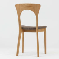 Niels Koefoedが1957年にデザインし、現在はCaso Furnitureより復刻製作されているモデル「Peter」のダイニングチェアです。オーク材の美しい木目を活かしたフレームと、背もたれに大きく設けられたアーチ状の開口部が印象的で、軽やかさと構造的な強度を両立したデザインが特徴です。身体をやさしく受け止める背のラインと、適度なクッション性を備えた座面により、日常使いにおいても快適な座り心地を実現しています。素材の質感を活かしたシンプルな佇まいは、ダイニング空間に自然と馴染み、北欧ミッドセンチュリー期のデザインらしい温かみと洗練を感じさせる一脚です。