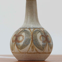 スーホルム・セラミック(Soholm Keramik)によるこちらのテーブルランプは、温かみのある陶磁器ベースに柔らかなブラウンとブルーで描かれた連続模様が印象的で、どこか手仕事の息づかいを感じさせる北欧ビンテージらしい魅力を備えています。丸みを帯びたベースからすっと伸びる首部のラインが美しく、リネンシェードを通した穏やかな灯りが空間にやさしい陰影を生み出します。高さ35cmと日常使いしやすいサイズで、ベッドサイドやリビングのサイドテーブルにも程よく収まり、落ち着いたインテリアに自然に馴染む一台です。