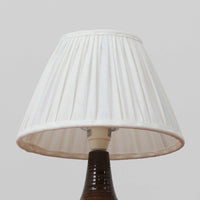 Soholm Keramik(スーホルム・セラミック)が手掛けたモデル1214のテーブルランプは、艶やかなブラウンの釉薬と段状のレリーフが生む豊かな表情が魅力で、陶磁器ならではの重量感と温かみが空間に落ち着いた存在感をもたらす北欧ビンテージ品です。柔らかな光を透過するリネンシェードがやさしい灯りを広げ、ベッドサイドやリビングのアクセント照明として取り入れやすく、経年の風合いが一層味わいを深めています。