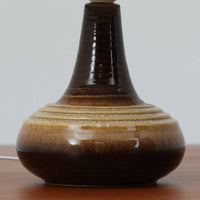 Soholm Keramik(スーホルム・セラミック)が手掛けたモデル1214のテーブルランプは、艶やかなブラウンの釉薬と段状のレリーフが生む豊かな表情が魅力で、陶磁器ならではの重量感と温かみが空間に落ち着いた存在感をもたらす北欧ビンテージ品です。柔らかな光を透過するリネンシェードがやさしい灯りを広げ、ベッドサイドやリビングのアクセント照明として取り入れやすく、経年の風合いが一層味わいを深めています。