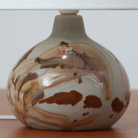 Soholm Keramik(スーホルム・セラミック)が手掛けたこちらのテーブルランプは、淡いグレーを基調にブラウンの流れるような釉薬模様が美しく広がる有機的な表情が魅力で、丸みを帯びた陶磁器のベースが空間にやさしい存在感をもたらす北欧ビンテージ品です。リネンシェードを透ける柔らかな灯りが落ち着いた雰囲気をつくり、ベッドサイドやリビングの間接照明として取り入れやすく、経年によって深まった色合いと一点物ならではの味わいを長く楽しめる一台です。