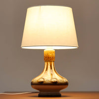 Soholm Keramik(スーホルム・セラミック)が手掛けたこちらのテーブルランプは、柔らかなクリーム色を基調にブラウンの縦流れ模様と円形のレリーフ装飾があしらわれた温かみある陶磁器ベースが魅力で、ふっくらと広がるフォルムが北欧ビンテージらしいやさしい存在感を放つ一台です。リネンシェード越しに灯る穏やかな光はベッドサイドやリビングの間接照明として心地よく空間を包み込み、経年で深まった釉薬の表情が一点物ならではの味わいを引き立てています。