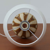 Soholm Keramik(スーホルム・セラミック)が手掛けたこちらのテーブルランプは、柔らかなクリーム色を基調にブラウンの縦流れ模様と円形のレリーフ装飾があしらわれた温かみある陶磁器ベースが魅力で、ふっくらと広がるフォルムが北欧ビンテージらしいやさしい存在感を放つ一台です。リネンシェード越しに灯る穏やかな光はベッドサイドやリビングの間接照明として心地よく空間を包み込み、経年で深まった釉薬の表情が一点物ならではの味わいを引き立てています。