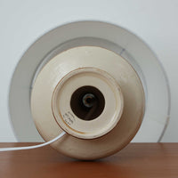 Soholm Keramik(スーホルム・セラミック)が手掛けたこちらのテーブルランプは、柔らかなクリーム色を基調にブラウンの縦流れ模様と円形のレリーフ装飾があしらわれた温かみある陶磁器ベースが魅力で、ふっくらと広がるフォルムが北欧ビンテージらしいやさしい存在感を放つ一台です。リネンシェード越しに灯る穏やかな光はベッドサイドやリビングの間接照明として心地よく空間を包み込み、経年で深まった釉薬の表情が一点物ならではの味わいを引き立てています。