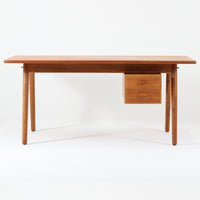 Poul M. Voltherがデザインし、FDB Moblerによって製作された片袖デスク。チーク材の天板と収納部、オーク材の脚部を組み合わせた構成に、真鍮の金具がさりげないアクセントを添える北欧ビンテージらしい一台です。幅160cmのゆとりあるサイズ感に対して、脚部や幕板は軽やかに設計されており、空間に圧迫感を与えません。片側に備えた引き出しユニットは、取り付けた状態でもスライドさせて位置調整が可能で、左右どちら側にも付け替えられる柔軟な構造となっています。さらに引き出しを取り外すことで、デスクとしてだけでなくダイニングテーブルとしても使用でき、暮らしの変化に合わせた使い方ができる点も魅力です。素材ごとの質感の違いと、経年により深みを増した木肌の表情が調和した、長く使い続けたくなるデザインです。