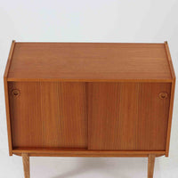 スウェーデン製のこちらのオープンシェルフは、チーク材の温かな木目とオーク材の脚部を組み合わせた軽やかな佇まいが魅力で、上段の棚板と下段のスライド扉収納を備えた実用性の高い構成が特徴の北欧ビンテージ家具です。丸い掘り込み取手や細身のフレームなど繊細なディテールが空間を柔らかく彩り、本や雑貨、食器などを美しく見せながら整頓でき、経年で深まった木肌の風合いがインテリアに落ち着きと温もりを与える一台です。