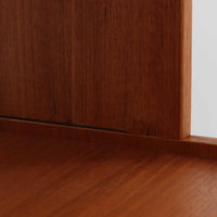 スウェーデン製のこちらのオープンシェルフは、チーク材の温かな木目とオーク材の脚部を組み合わせた軽やかな佇まいが魅力で、上段の棚板と下段のスライド扉収納を備えた実用性の高い構成が特徴の北欧ビンテージ家具です。丸い掘り込み取手や細身のフレームなど繊細なディテールが空間を柔らかく彩り、本や雑貨、食器などを美しく見せながら整頓でき、経年で深まった木肌の風合いがインテリアに落ち着きと温もりを与える一台です。